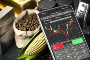 mobile phone showing a commodities trading platform sits next to real life commodities